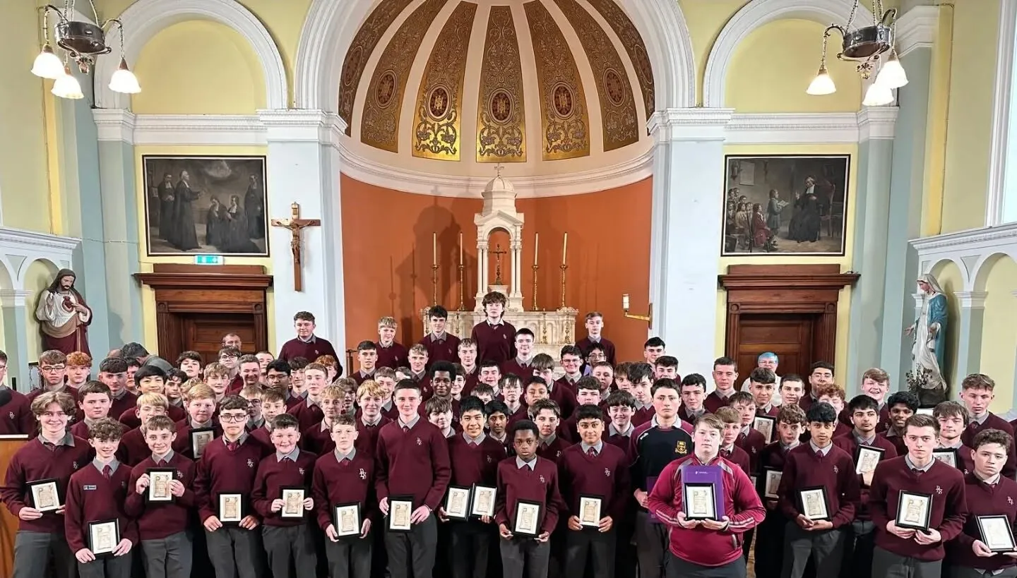 A large group of students in the college chapel, each holding a certificate, in front of the altar