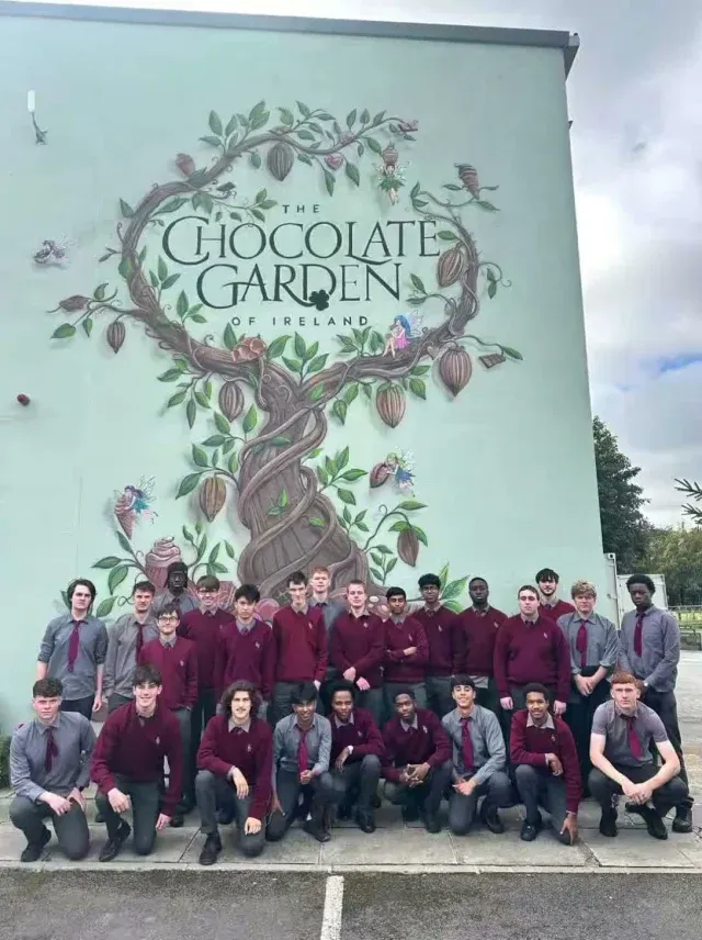 A large group of De La Salle students in maroon jumpers in front of a tree mural at the Chocolate Garden