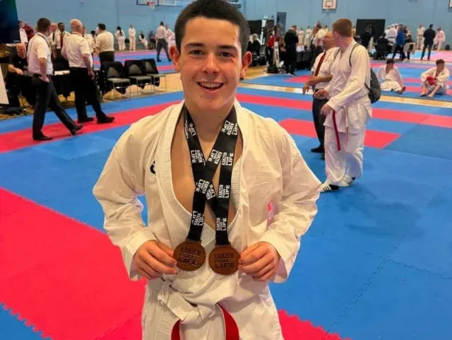 A De La Salle student holding three medals on a judo mat