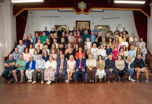 A large group photograph of De La Salle College staff in a hall